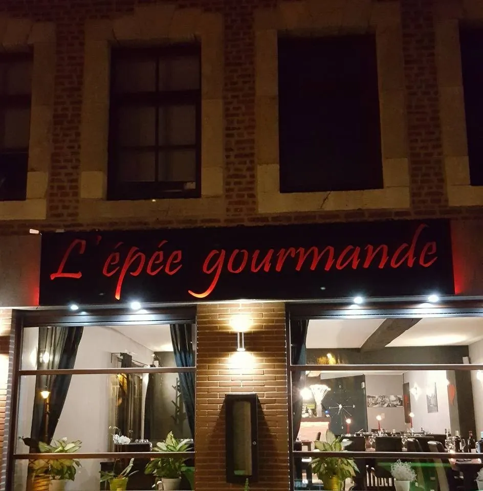 L’enseigne rouge « L’épée gourmande » allumée sur la façade, la nuit