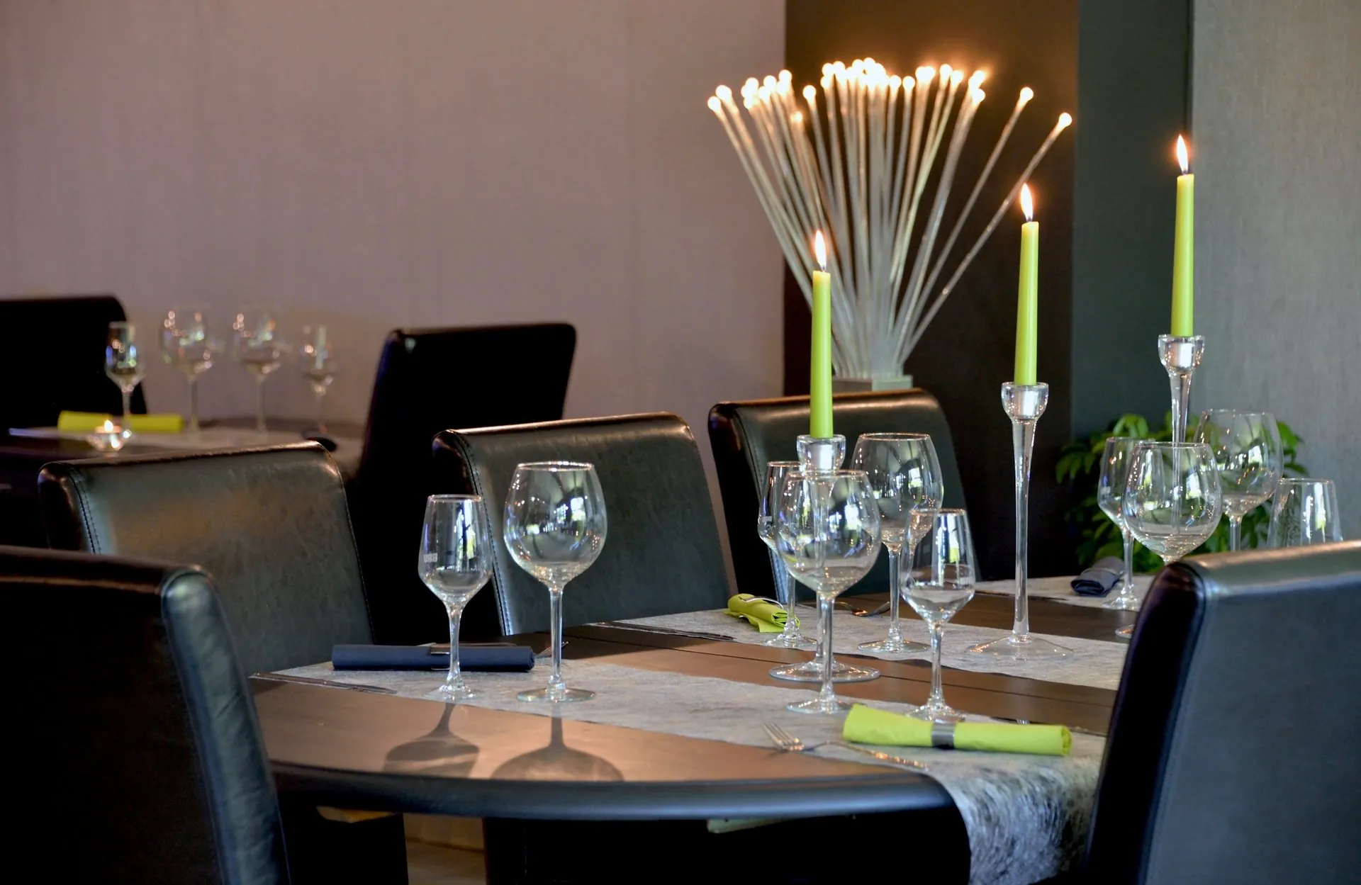 Table dressée en salle, verres alignés et bougies vertes allumées